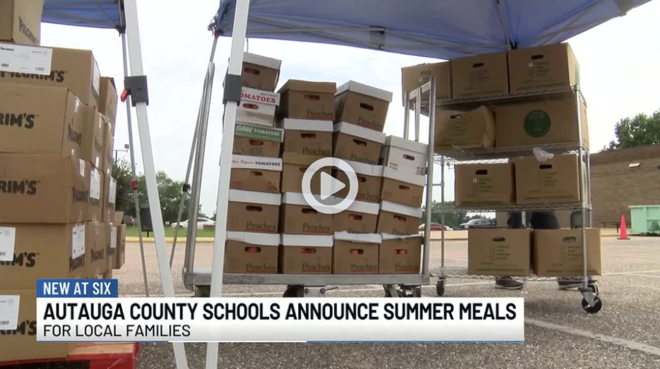 WSFA 12 News broadcast still captioned Autauga County Schools announce summer meals for local families, showing stacked cases of produce and food boxes on carts under a canopy