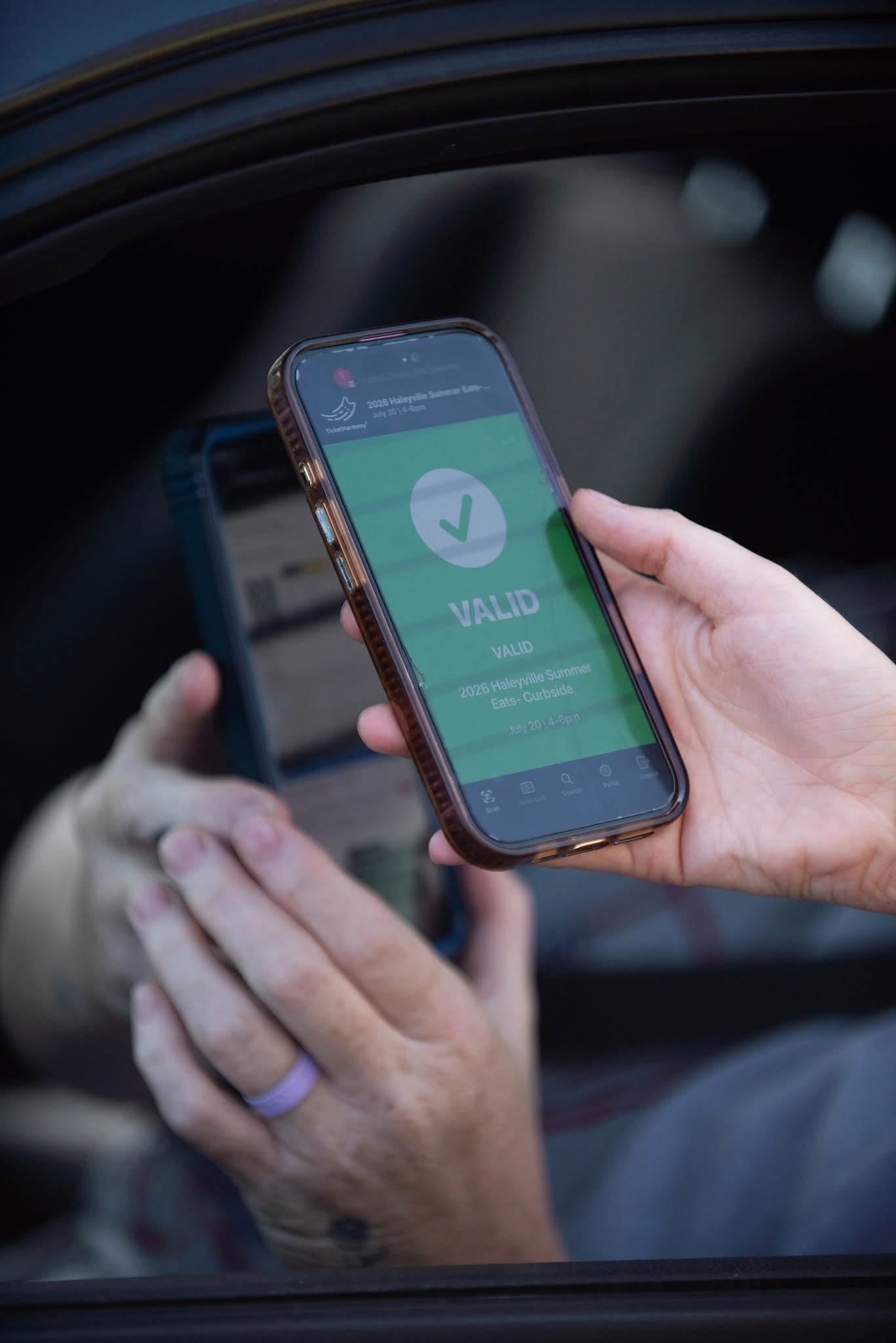 A phone showing a green VALID scan result for the 2026 Haleyville Summer Eats curbside meal pickup, held at a car window